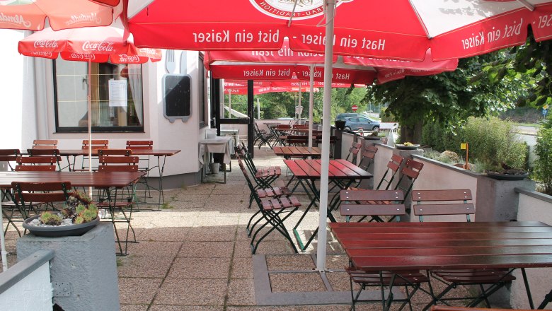 An empty guest garden with wooden tables and chairs under red parasols.