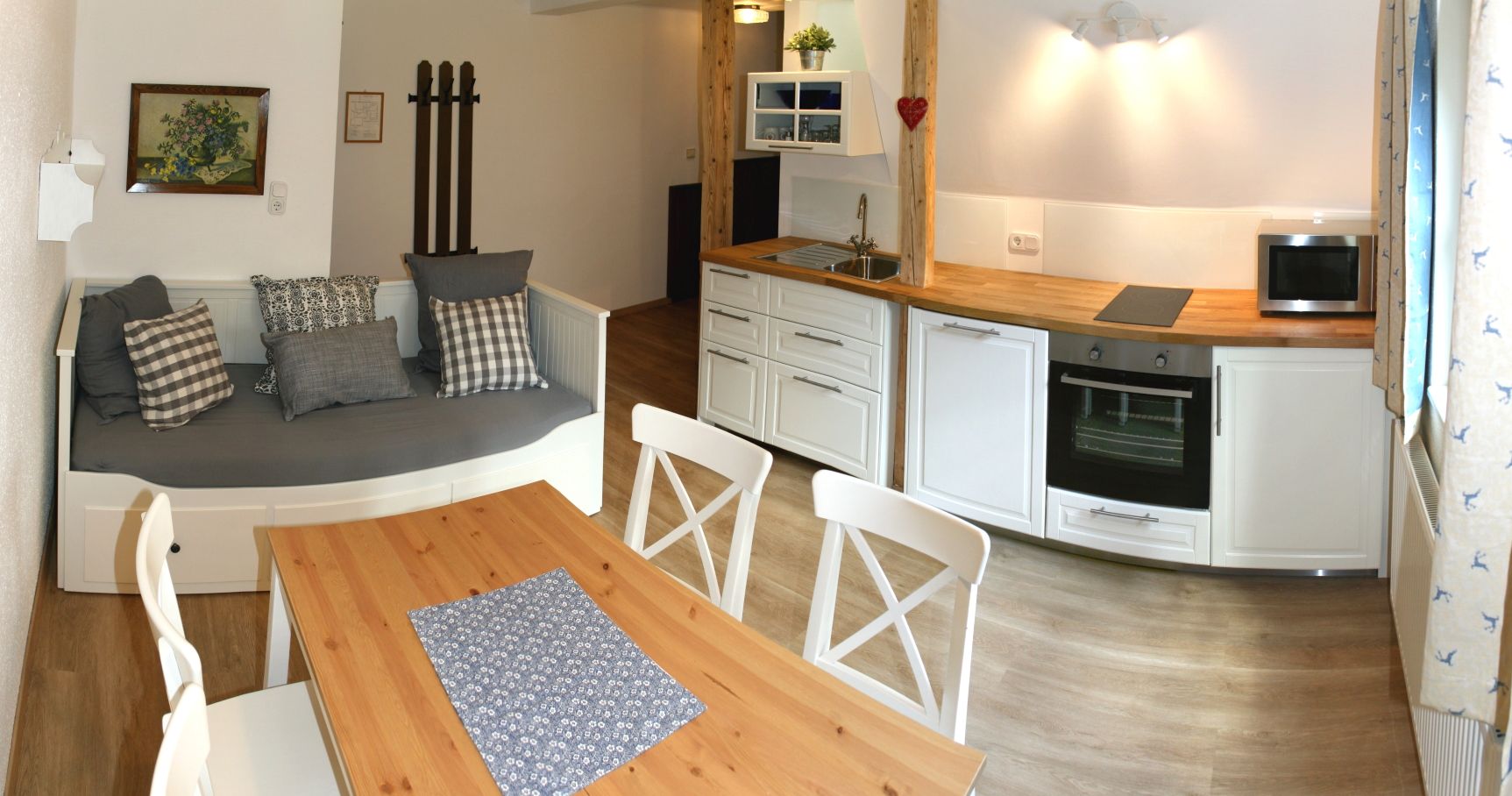 Cozy kitchen with wooden table, white chairs, sofa and modern kitchenette.