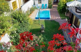 View of a garden with pool, surrounded by houses and red flowers in the foreground.