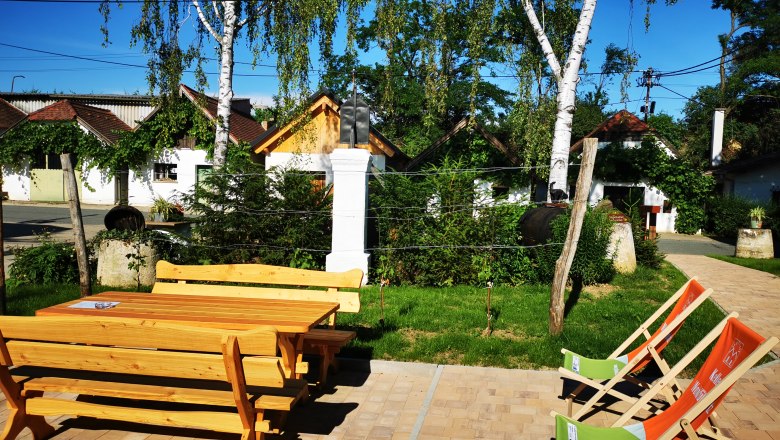 Wooden table and chairs outside with deckchairs, surrounded by trees and small buildings in Hadres.