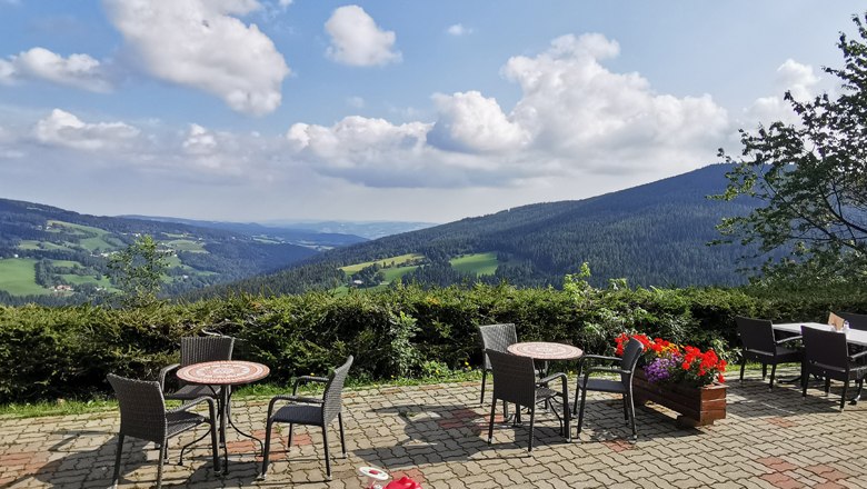 Terrace with tables and chairs, view of green hills and blue sky with clouds.