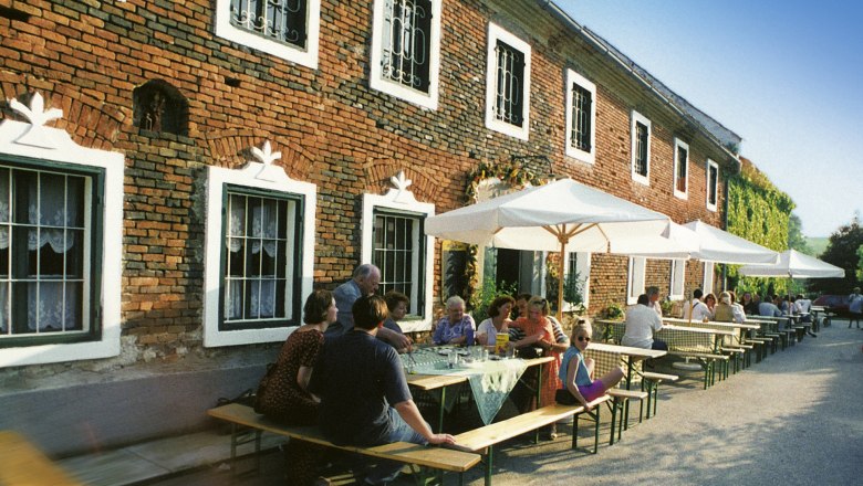 People sit at tables in front of a brick building with parasols.
