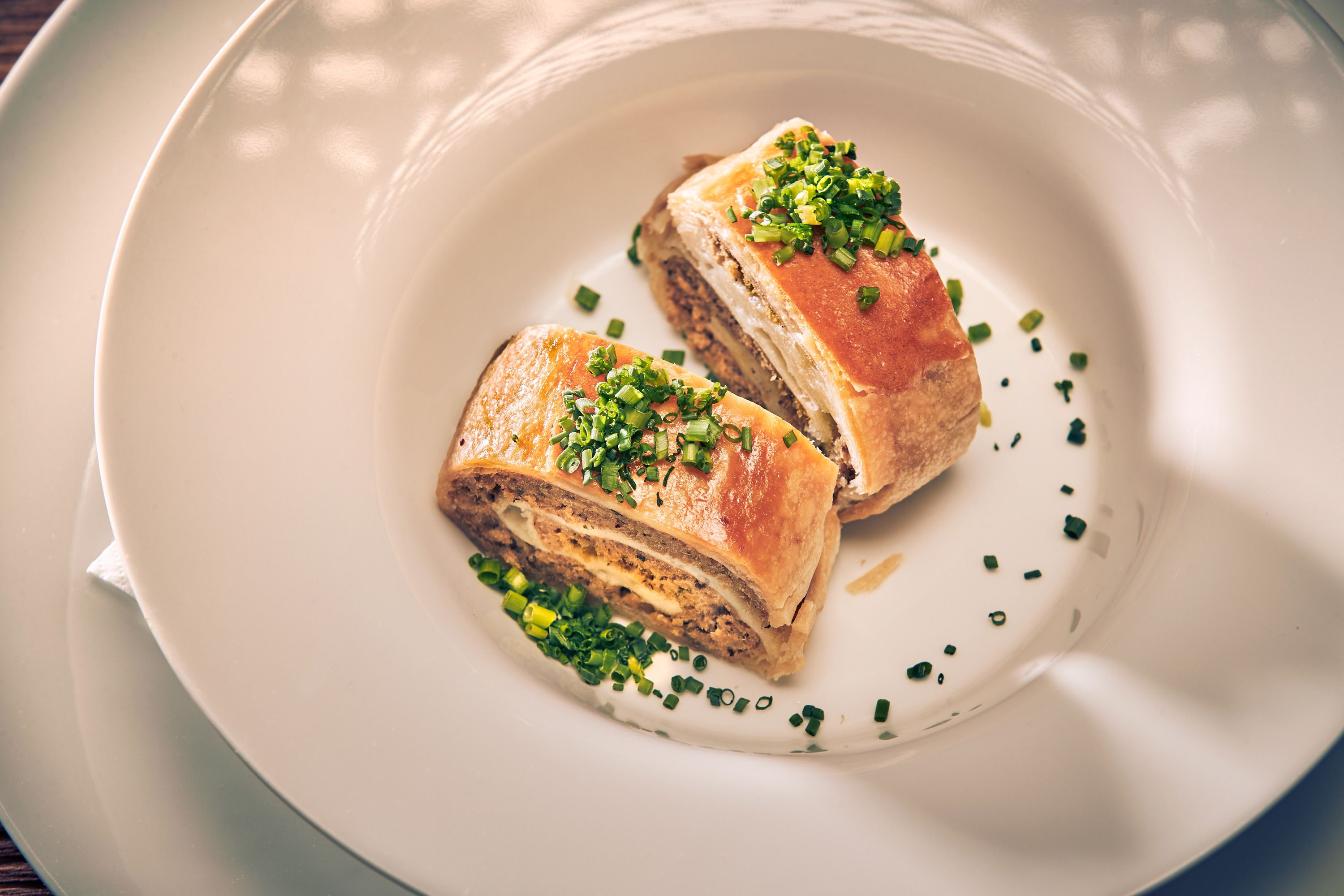 Two pieces of meat strudel served with chives on a white plate.