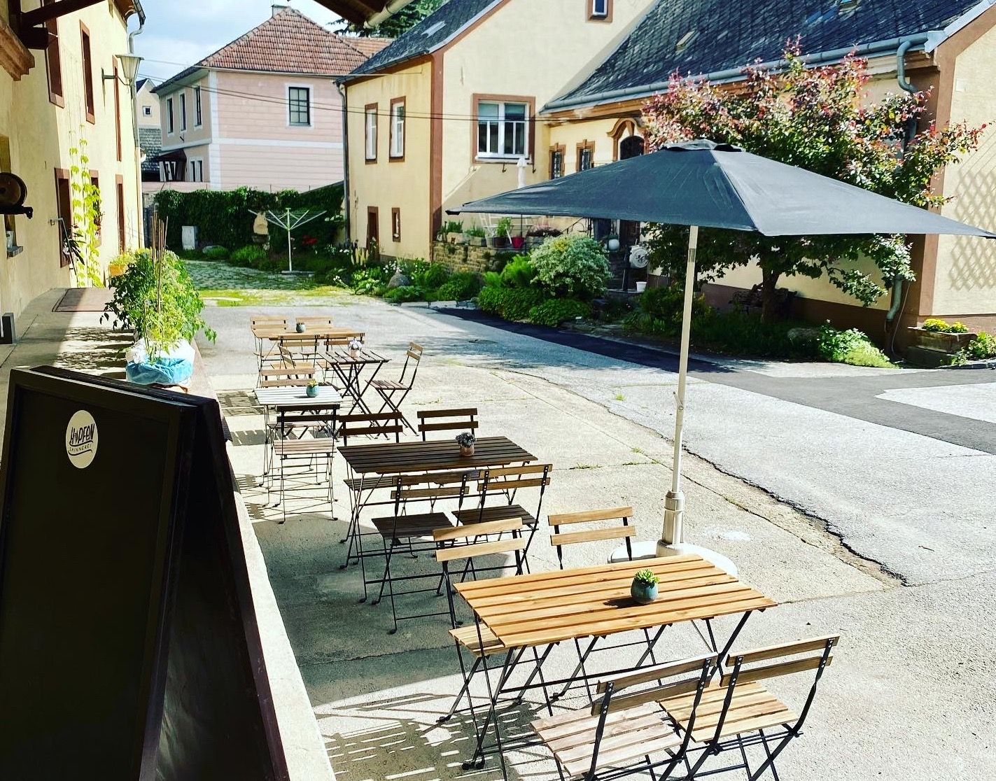 A guest garden with wooden tables and chairs, a parasol and plants in an inner courtyard.