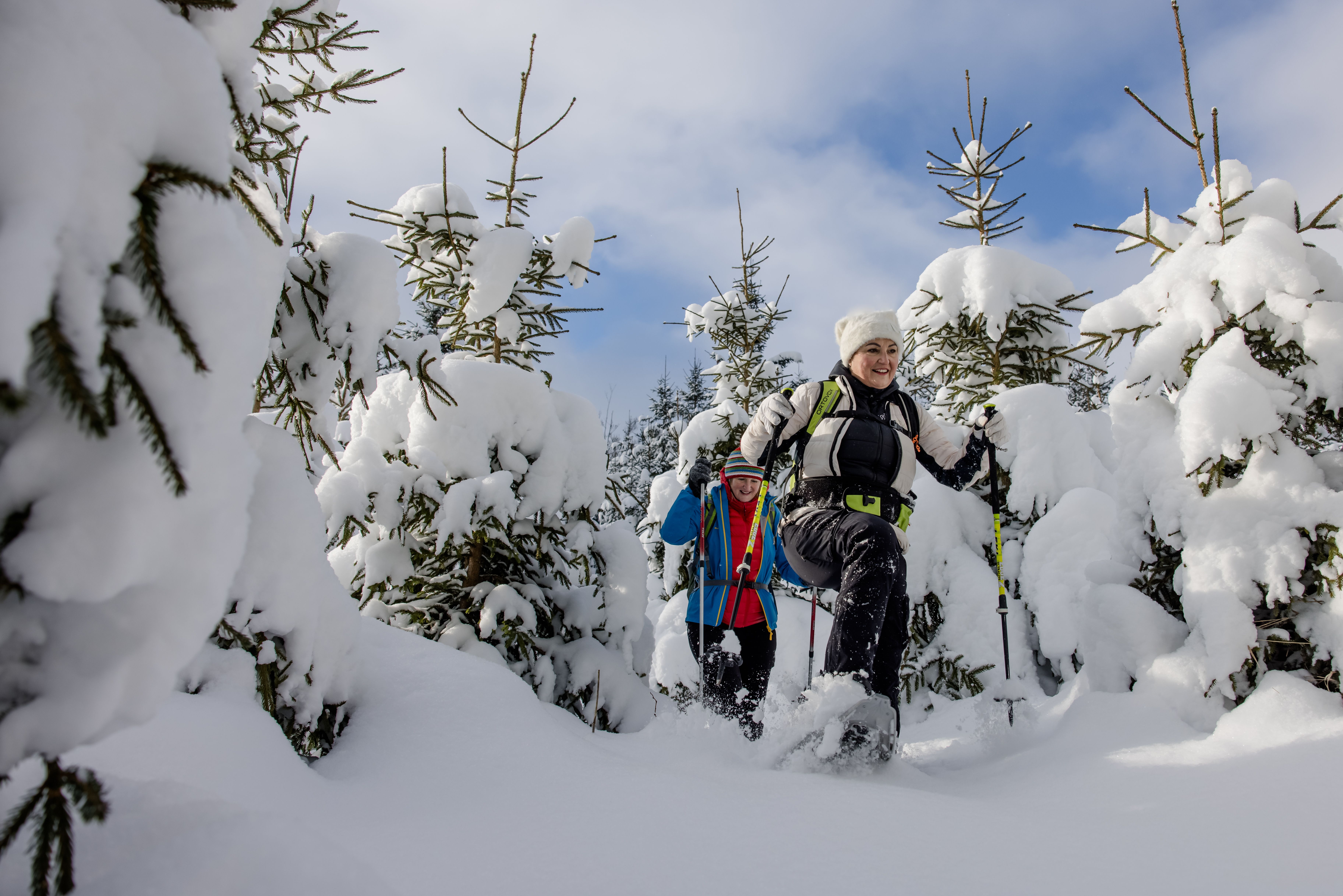 Two people snowshoeing in a snow-covered field under a clear sky.