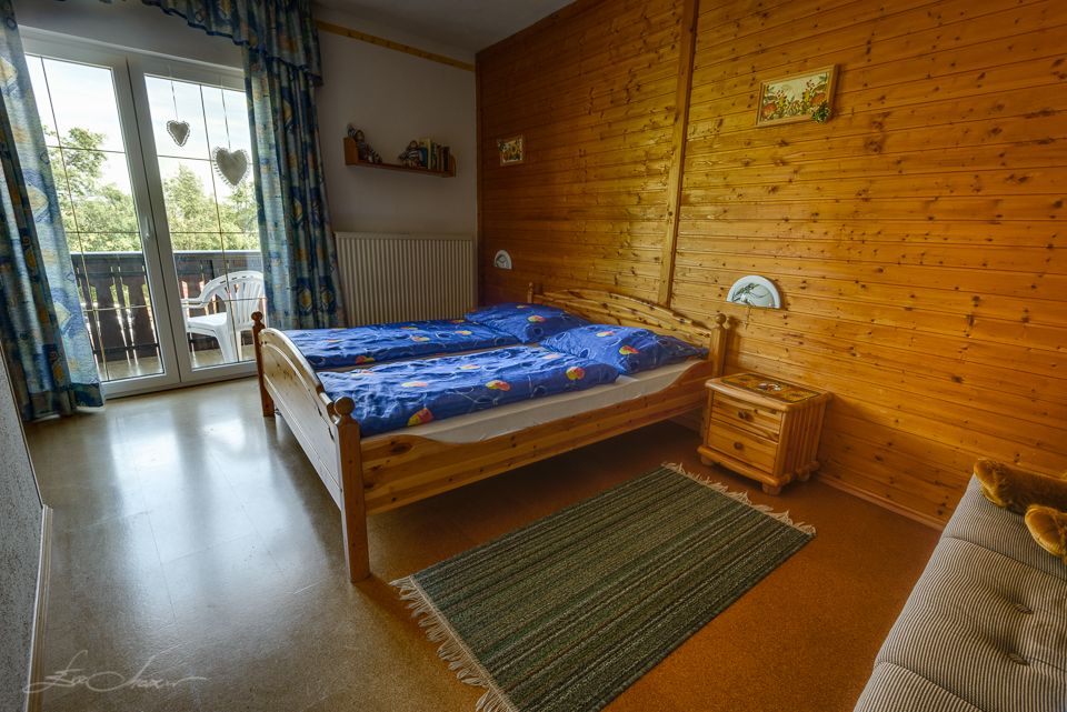 Cozy bedroom with wooden walls, double bed, blue bedding and balcony with a view of the countryside.