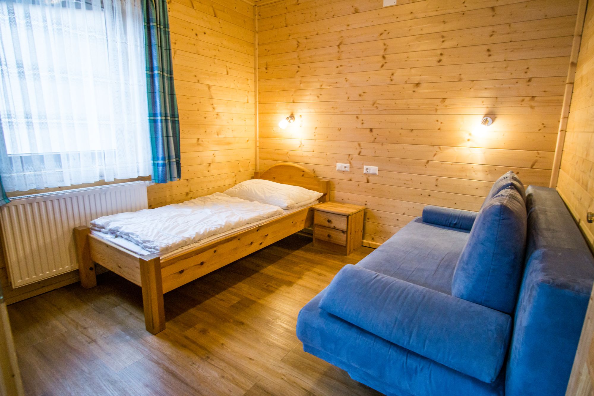 Children's room with wooden walls, single bed, blue sofa and bedside table.