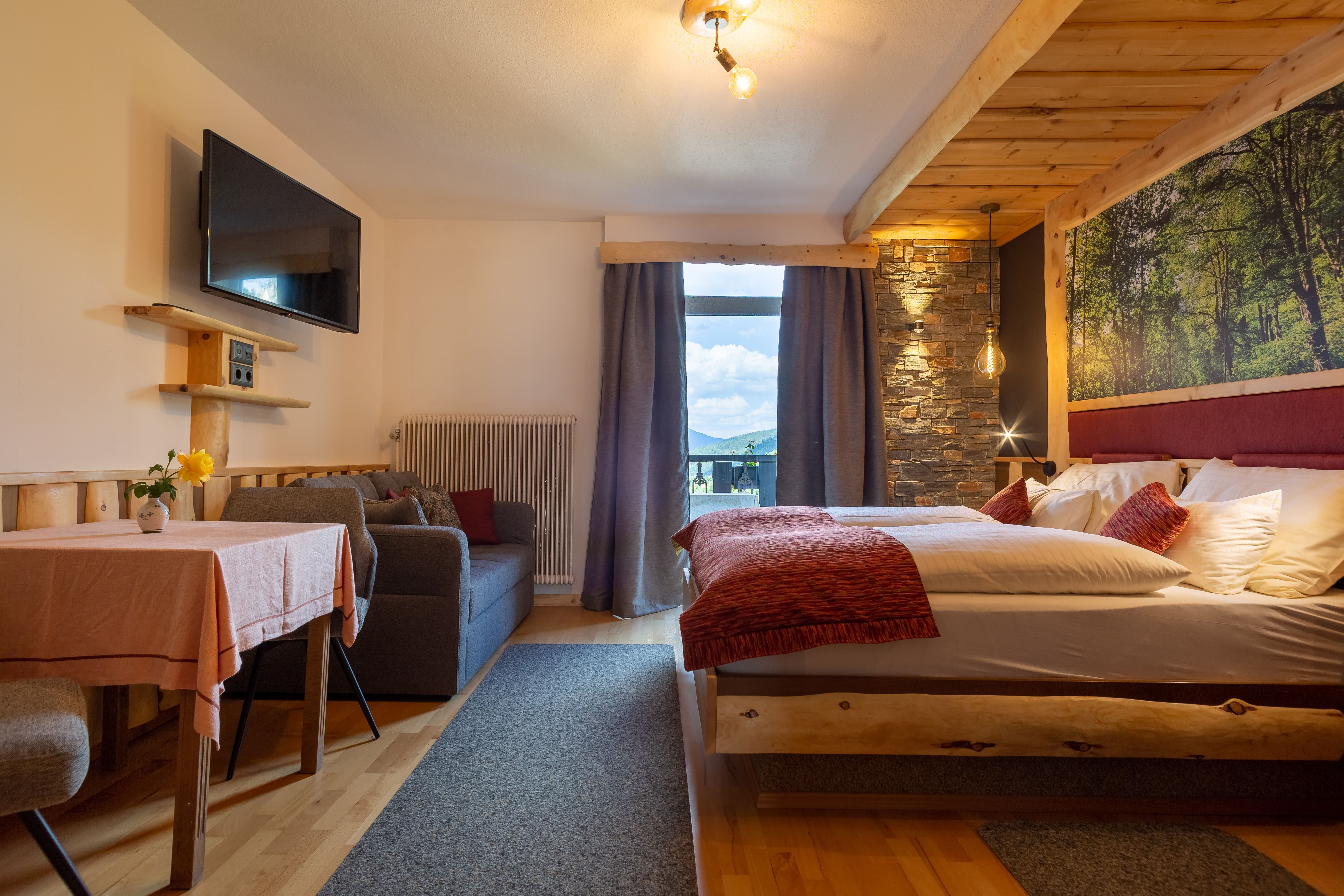 Comfortable hotel room with double bed, sofa, table and large window with mountain view.