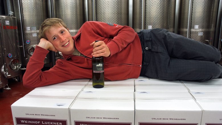 Person lying on wine cartons in the wine cellar, holding a wine bottle.