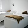 Two white beds in a bright room with brown blankets and pillows.