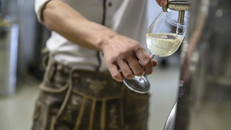 Person fills a glass with white drink from a stainless steel container.