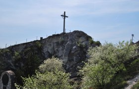 A cross stands on a hill with blossoming trees in the foreground.