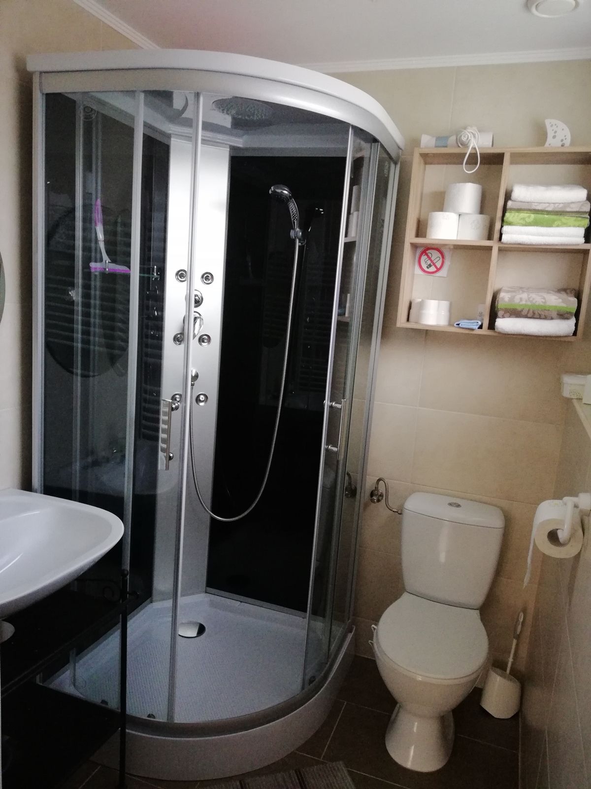 Modern bathroom with shower cubicle, washbasin, toilet and shelf with towels and toilet paper.
