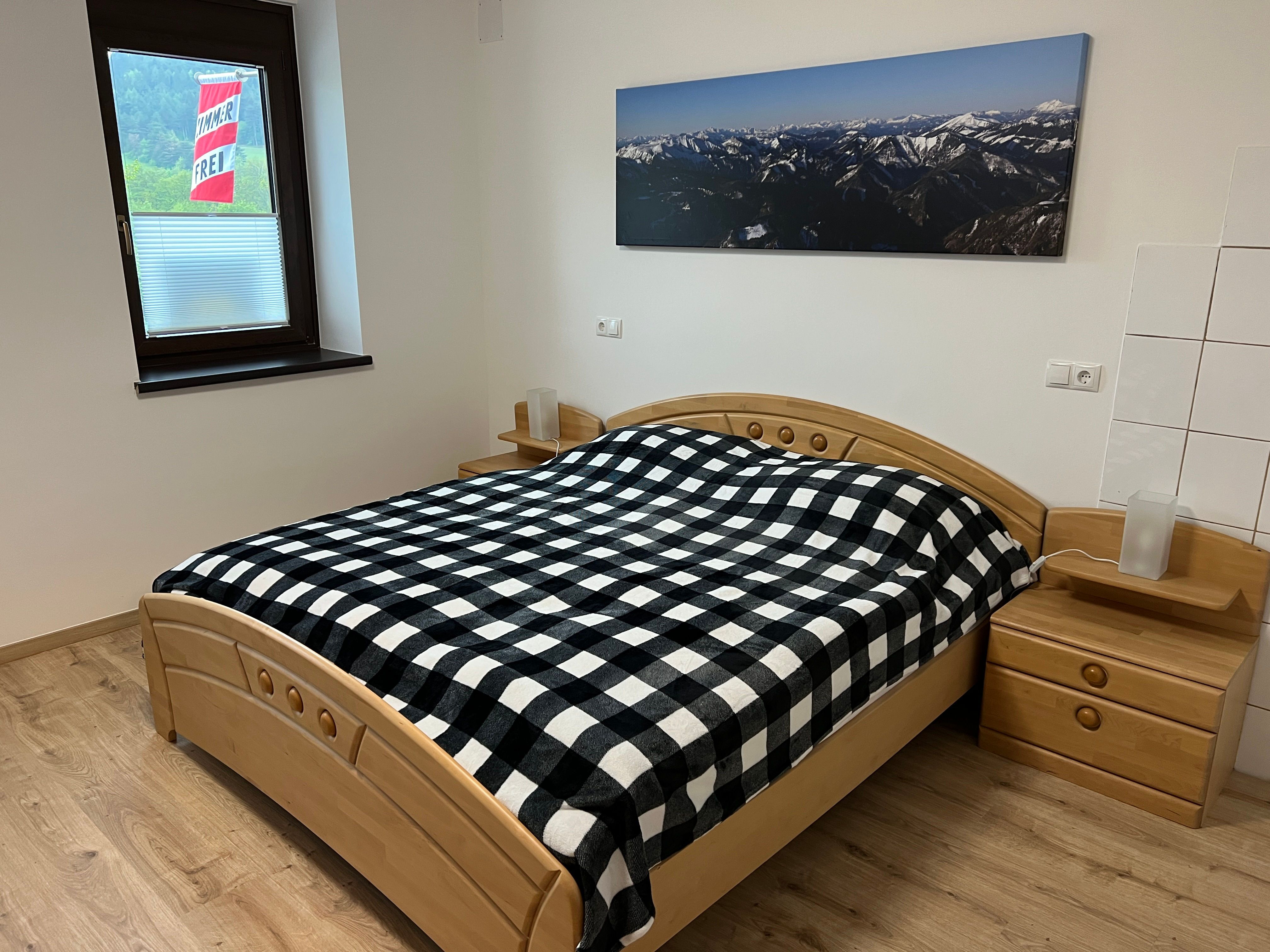 Bedroom with double bed, checkered comforter cover and mountain picture on the wall.