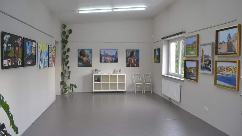 Interior view of a gallery with paintings on the walls and a shelf in the middle.