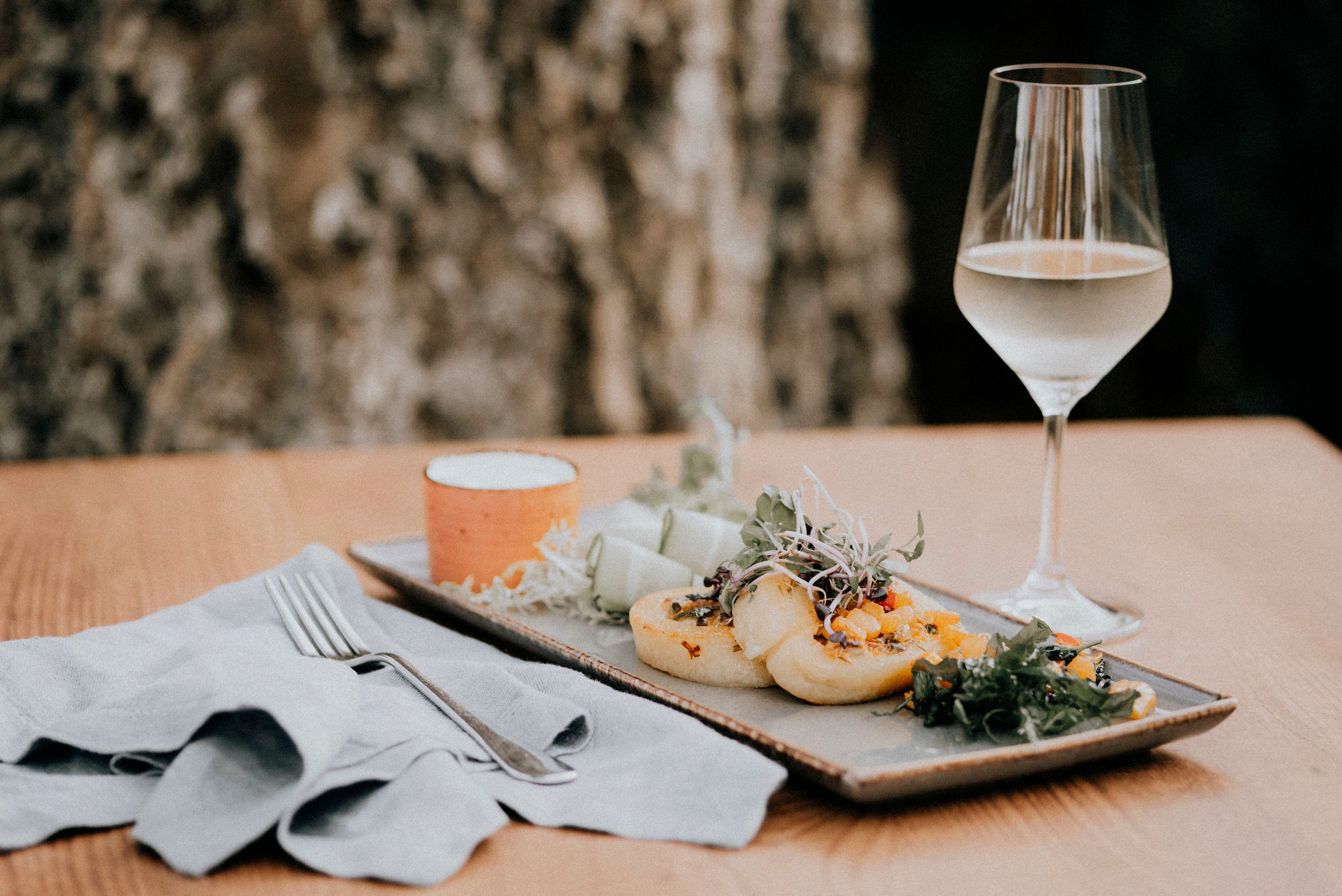 Potato roulade with pumpkin and sheep's cheese on a plate, with a glass of white wine next to it.