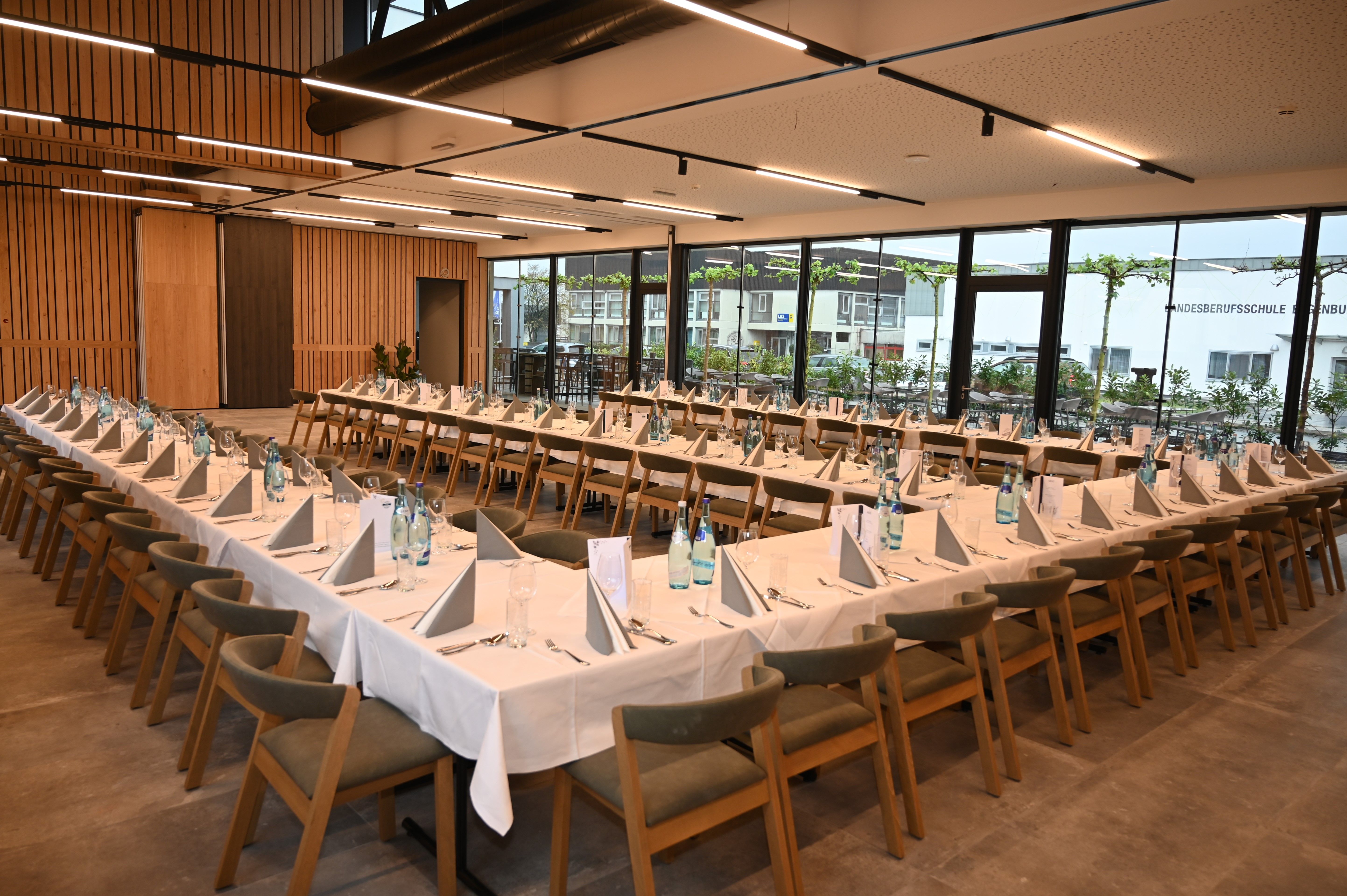 A large, modern seminar room with U-shaped tables, wooden chairs and large windows.