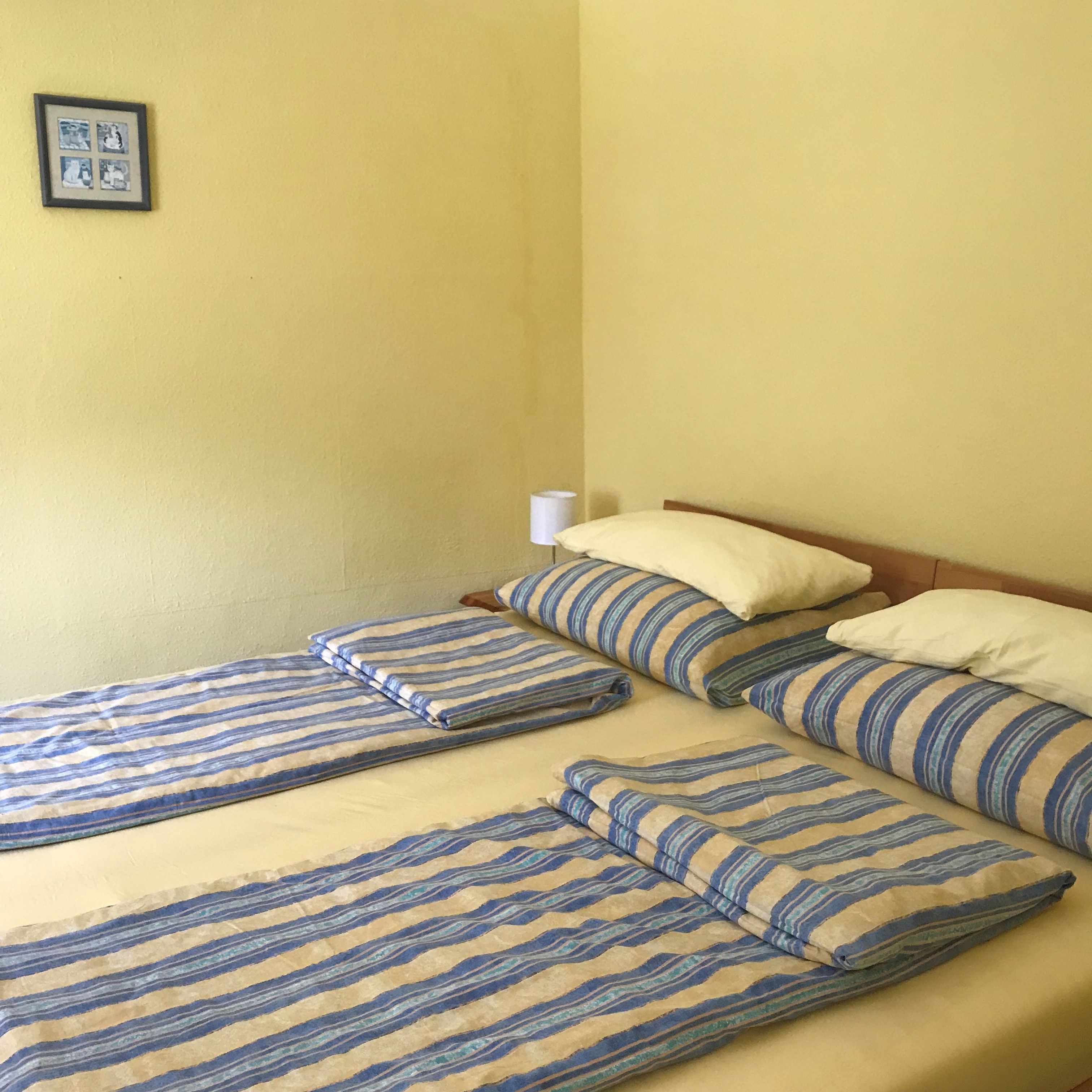 Bedroom with double bed, striped bed linen, yellow walls, small picture on the wall.