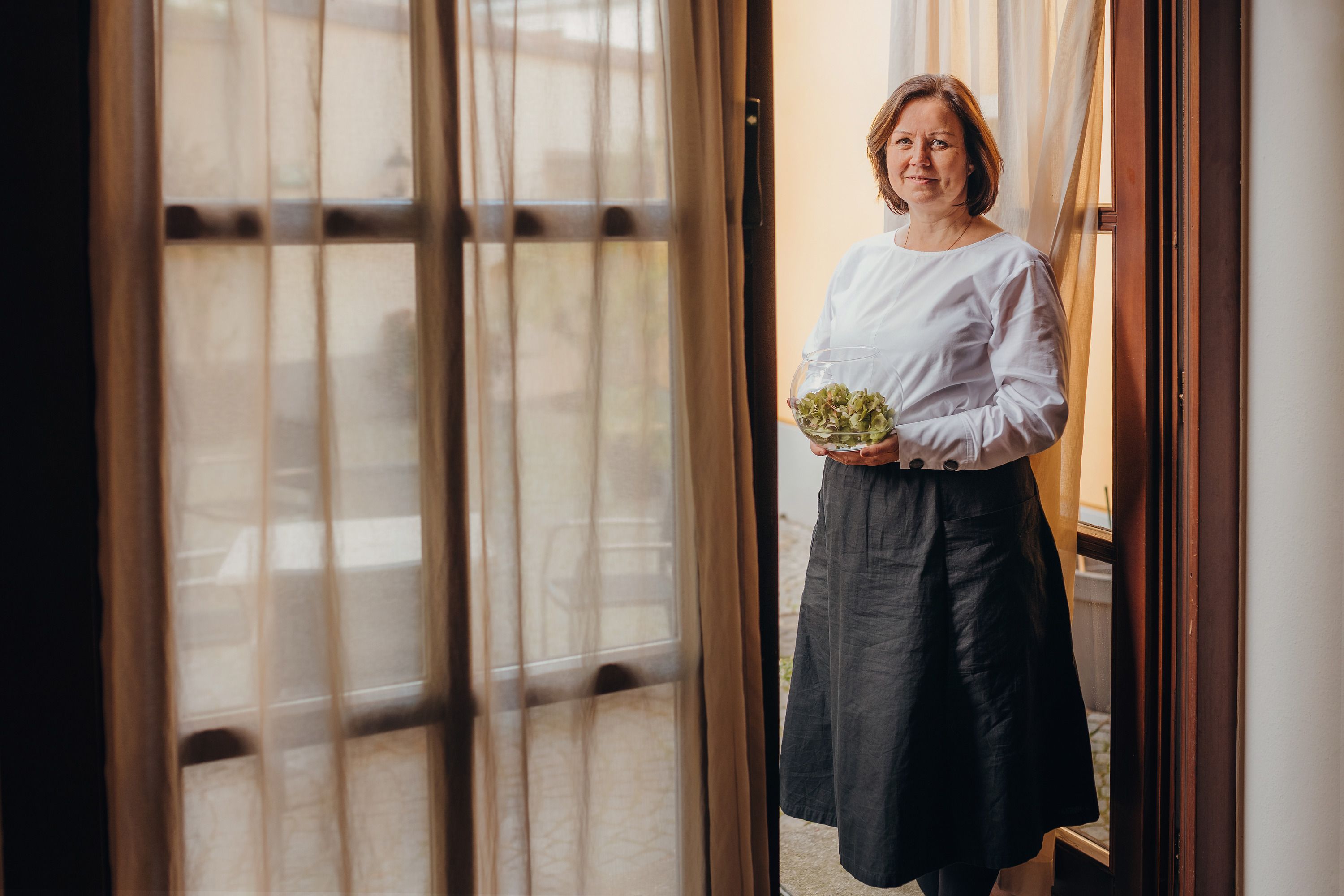 A woman stands in a doorway holding a bowl of salad.