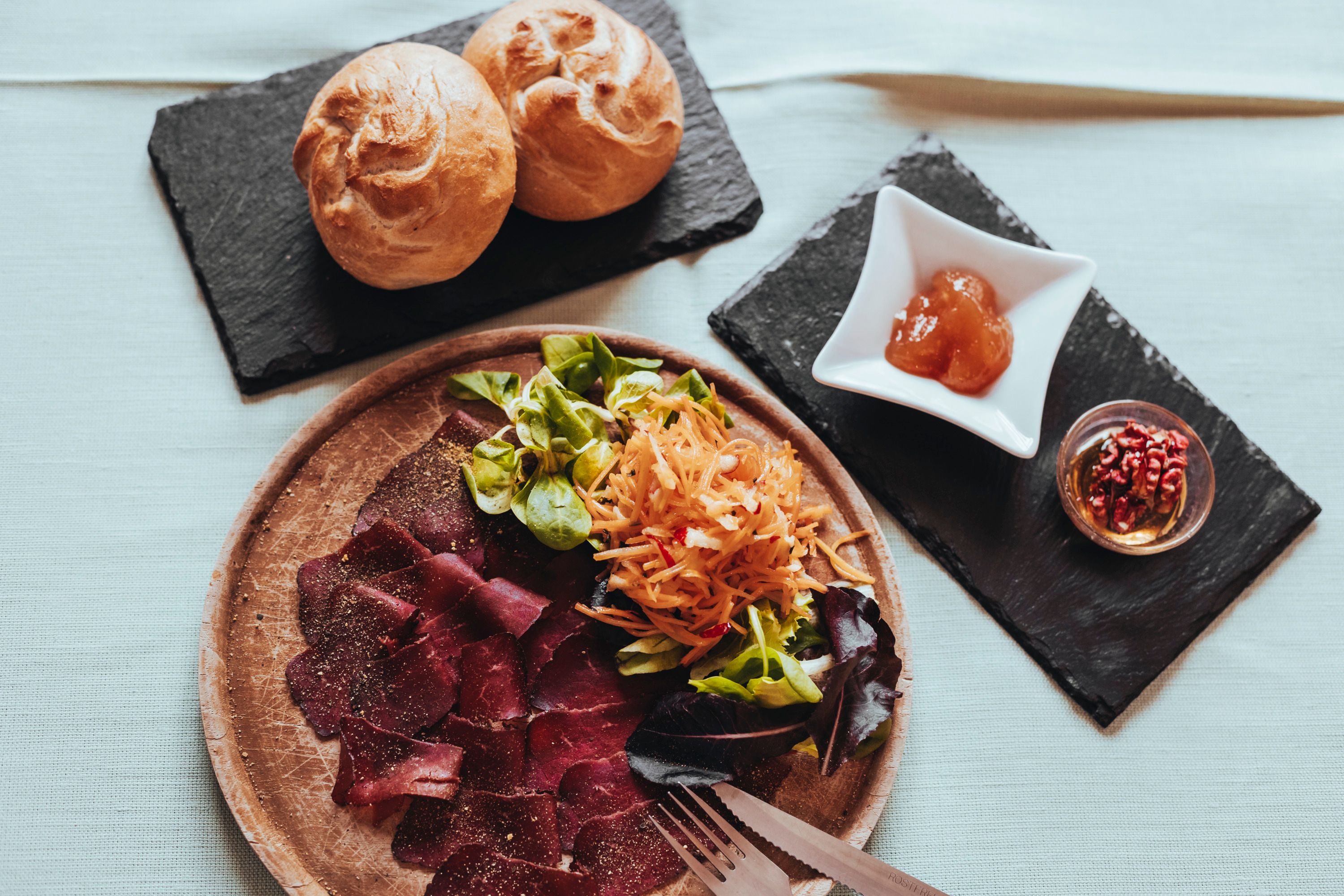 Plate with ham, salad and bread rolls on a table.