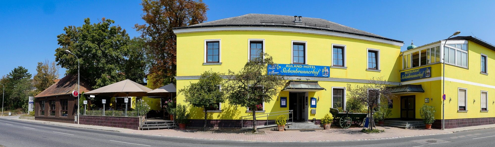 Yellow building with restaurant and hotel, surrounded by trees and road.