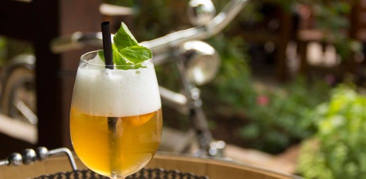 A glass with a sparkling drink and mint leaf on an outdoor table, a bicycle in the background.