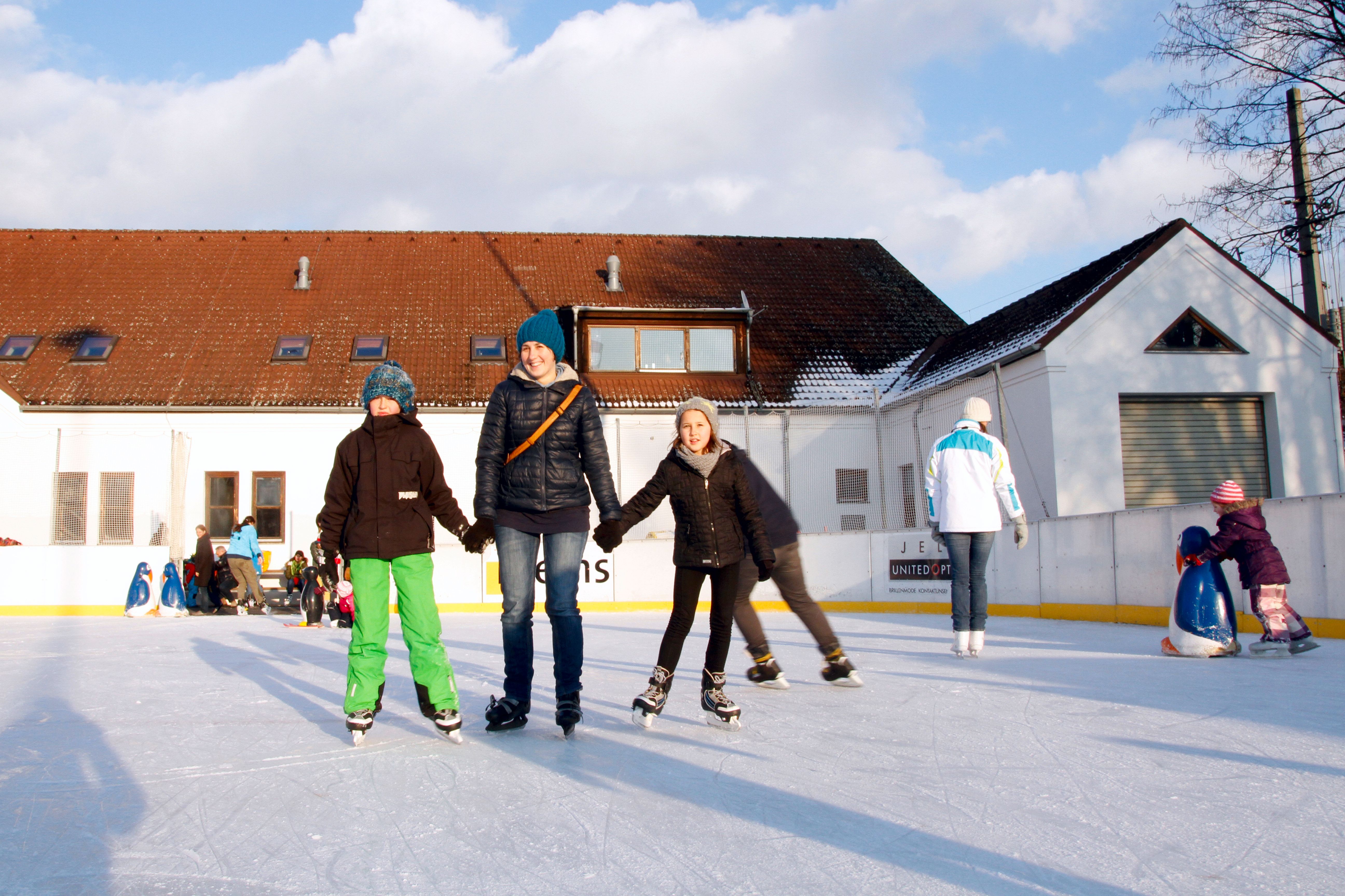 People skating on an artificial ice rink in front of a building.
