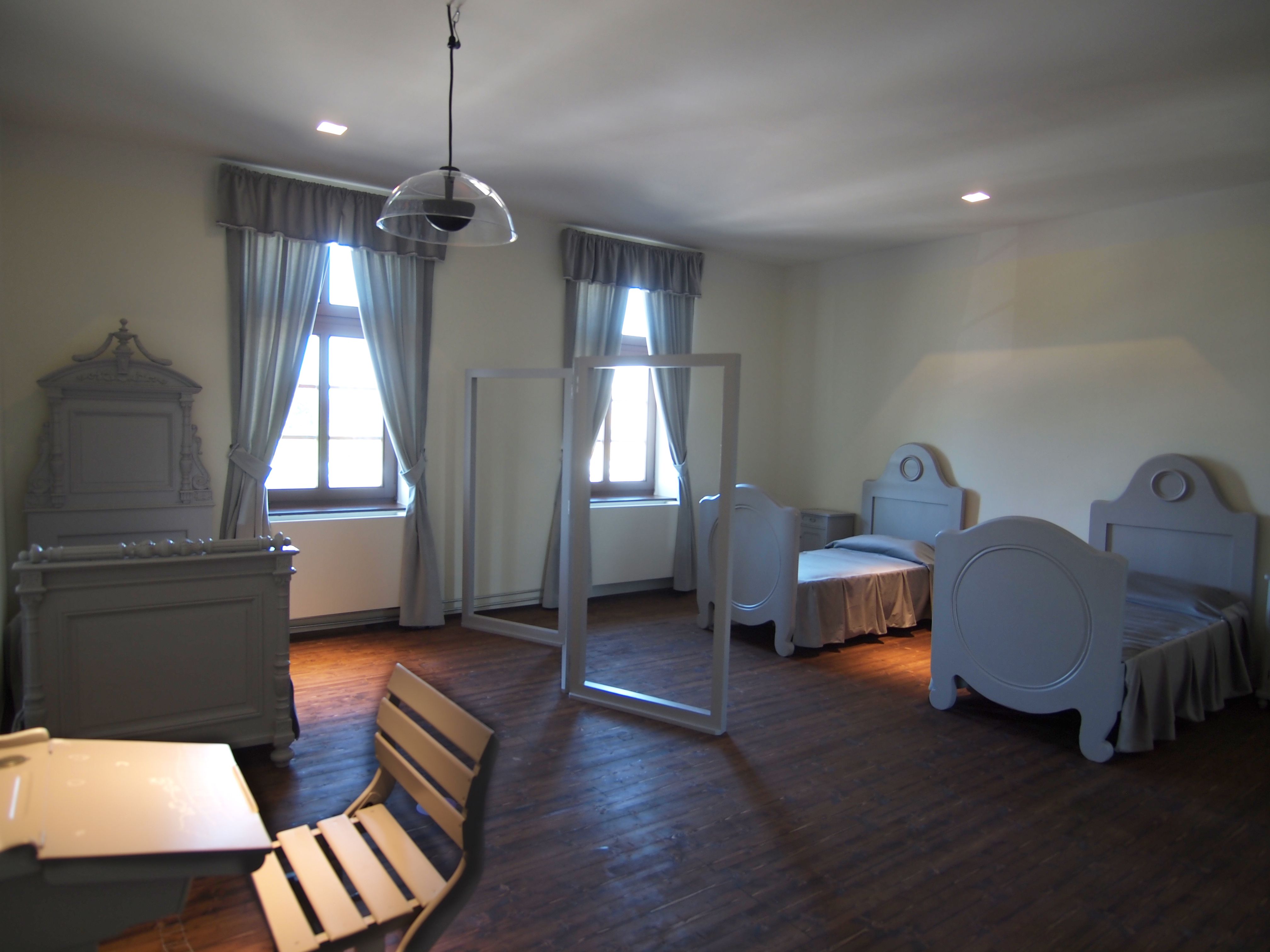 A simply furnished bedroom with two beds, a table and chairs, all in gray tones.