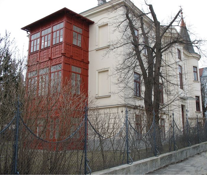 A historic building with a red bay window and a fence in the foreground.