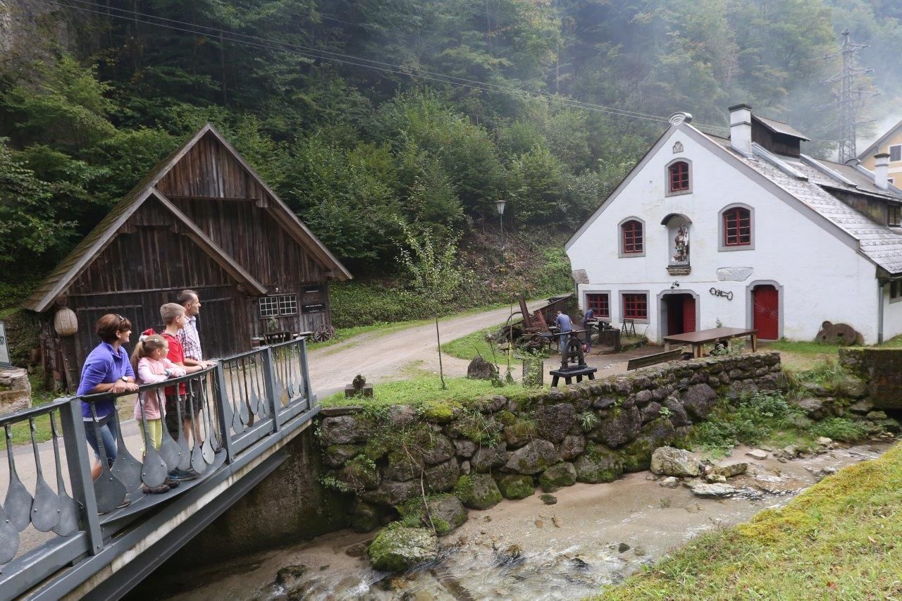 A family stands on a bridge in front of a historic building in a rural setting.