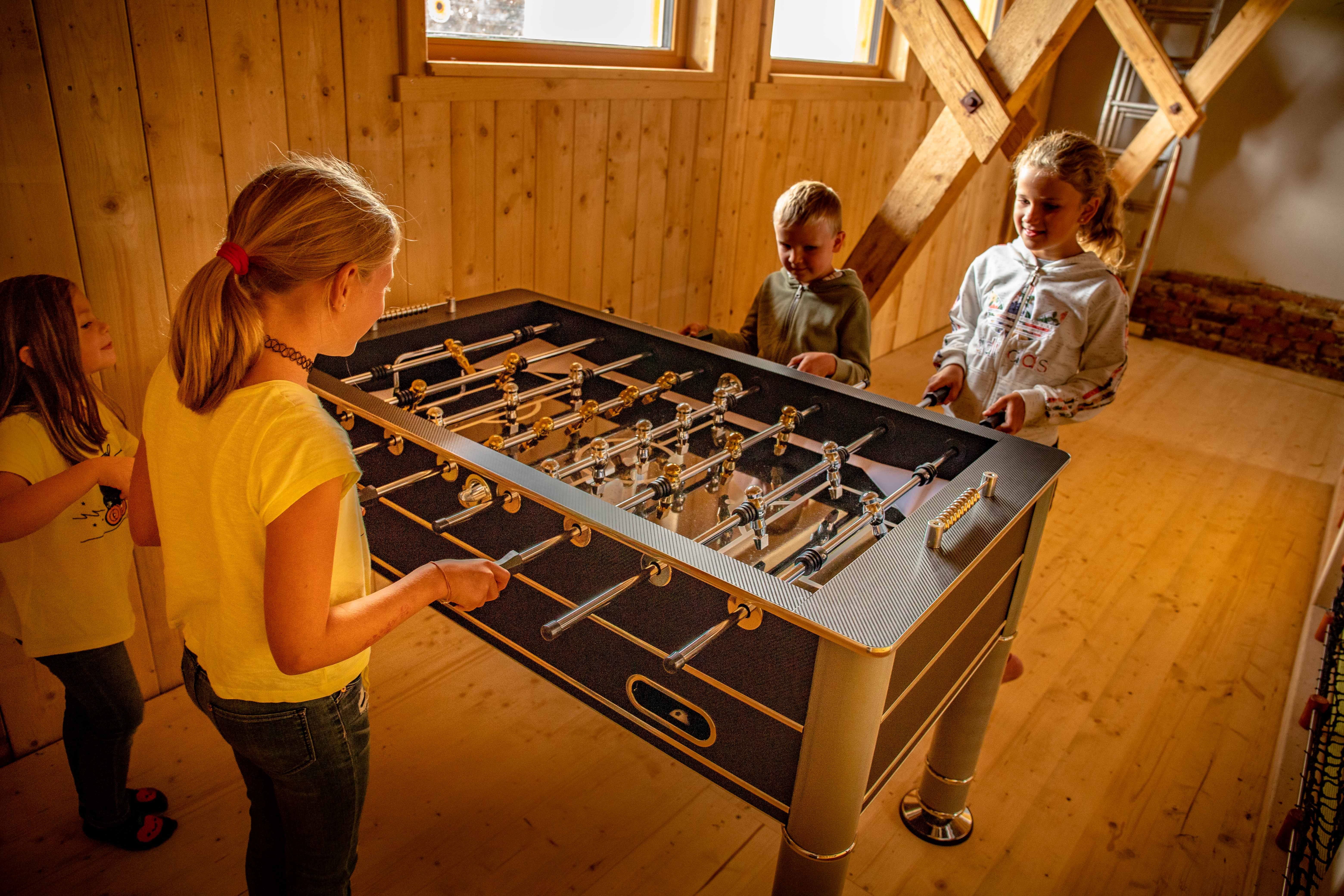 Children play table soccer in a wooden room.