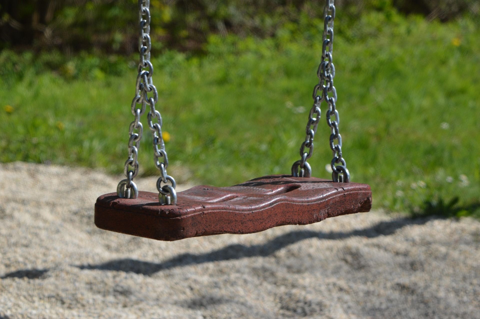Close-up of an empty wooden swing with metal chains hanging in a sunny garden.