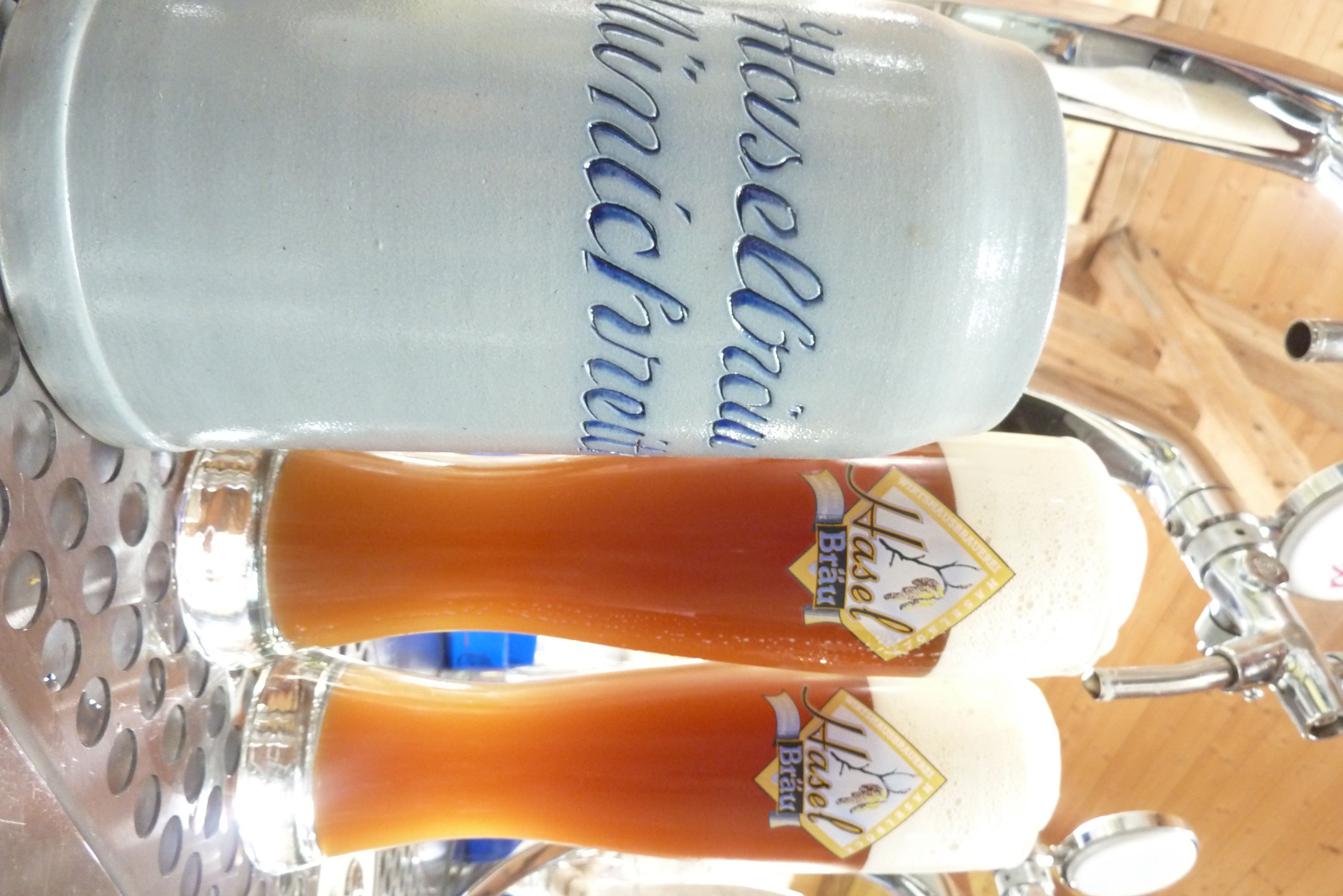 Two glasses of beer and a mug labeled 'Haselbräu Münichreith' on a counter.