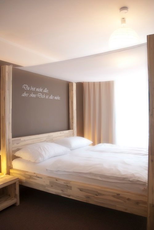 A four-poster bed in a bright room with a quote on the wall.