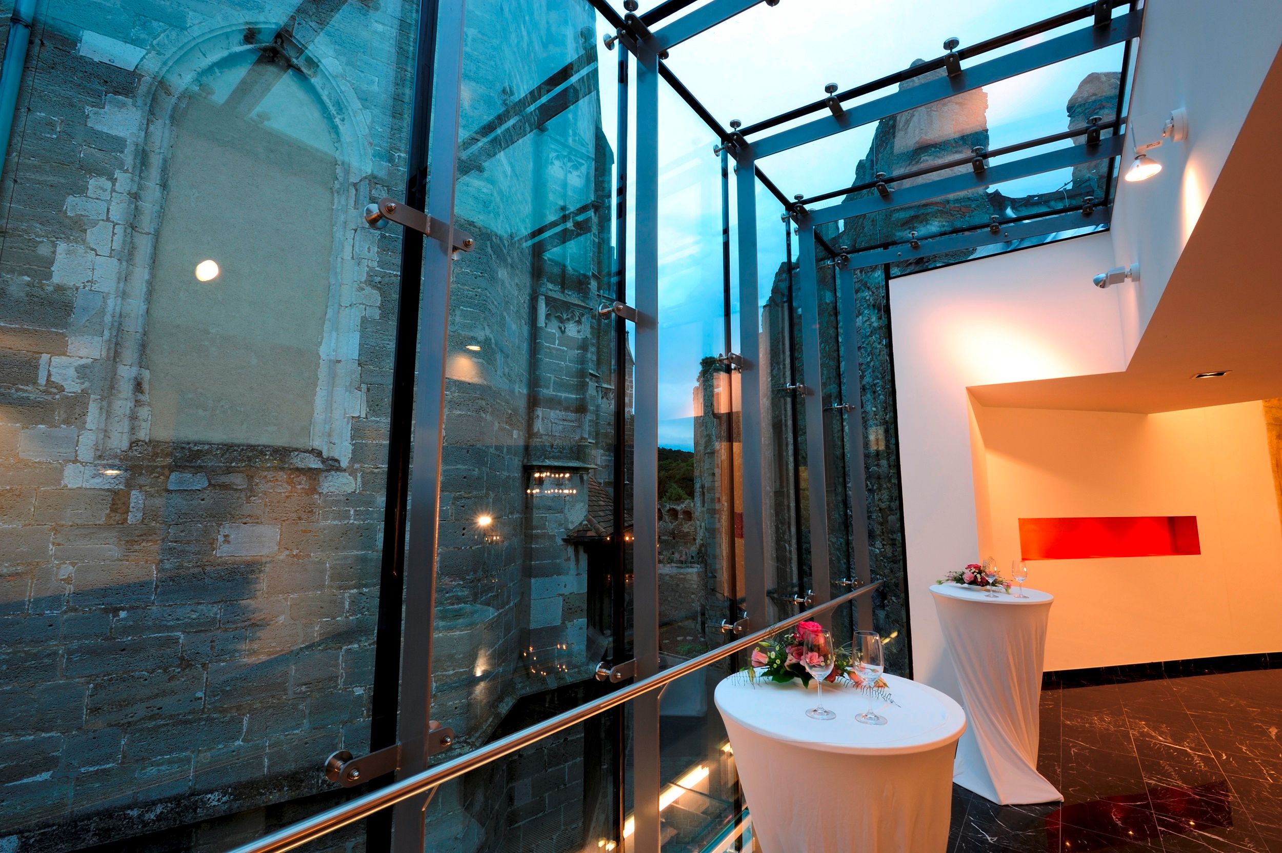 Modern glass architecture next to an old stone wall with decorated bar tables.