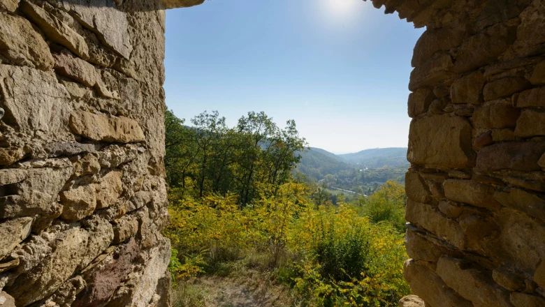 View through a stone wall of a hilly landscape with trees and blue sky.