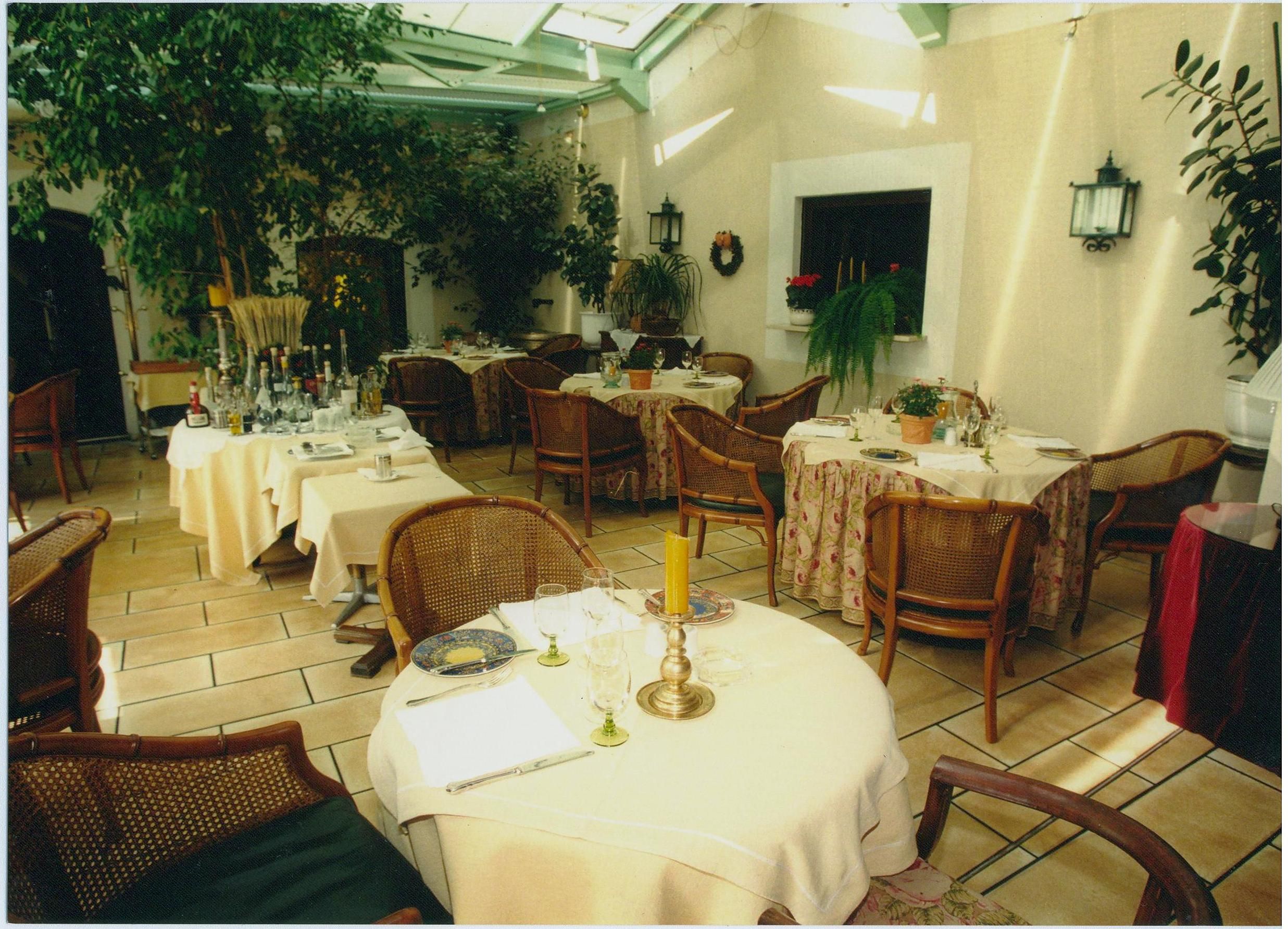 A cozy winter garden of a country hotel with laid tables, plants and wicker chairs.