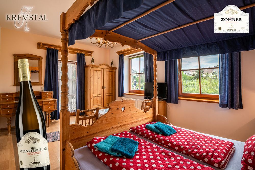 A cozy room with a four-poster bed, wooden furniture and a view of the vineyards. A bottle of wine is pictured in the foreground.