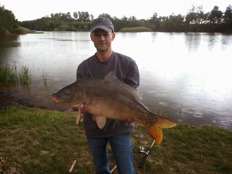A man holds a large fish in front of a lake.