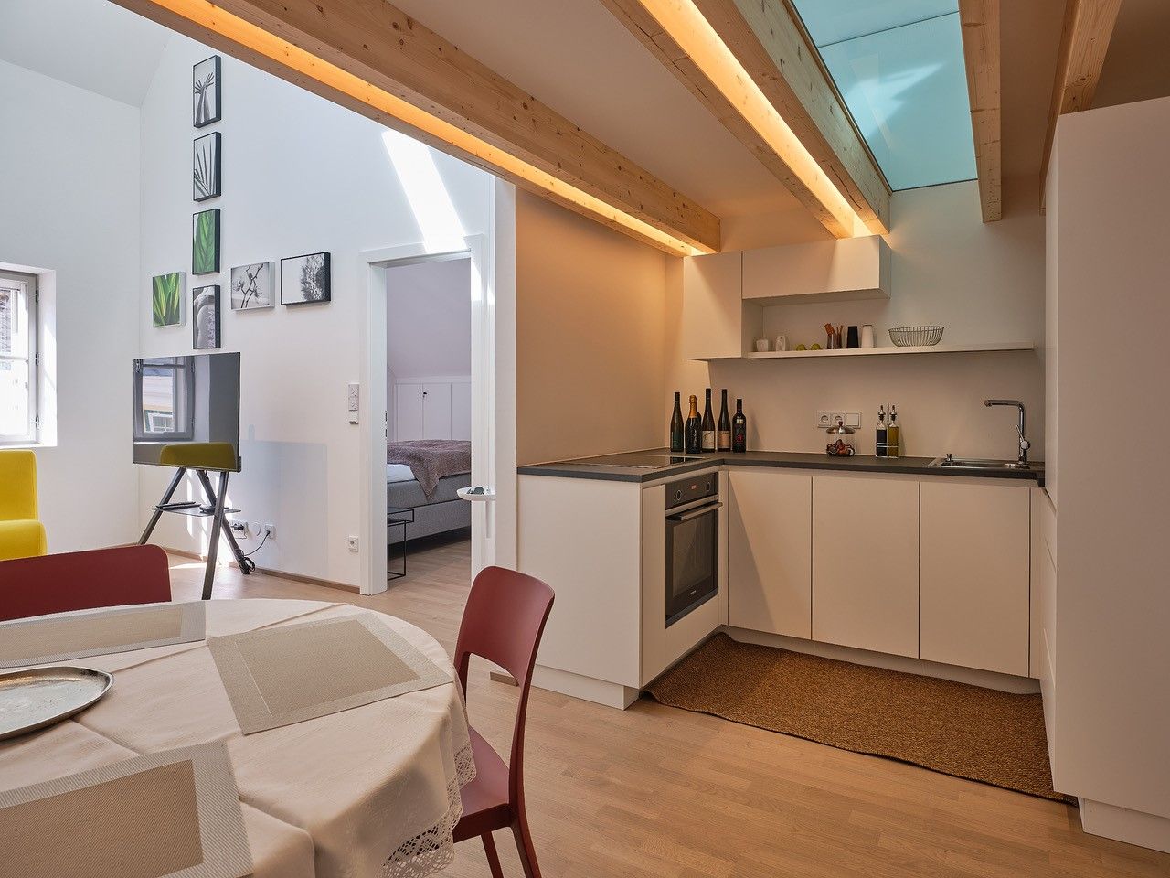 Modern kitchen with wooden beams, dining table and view into the bedroom.