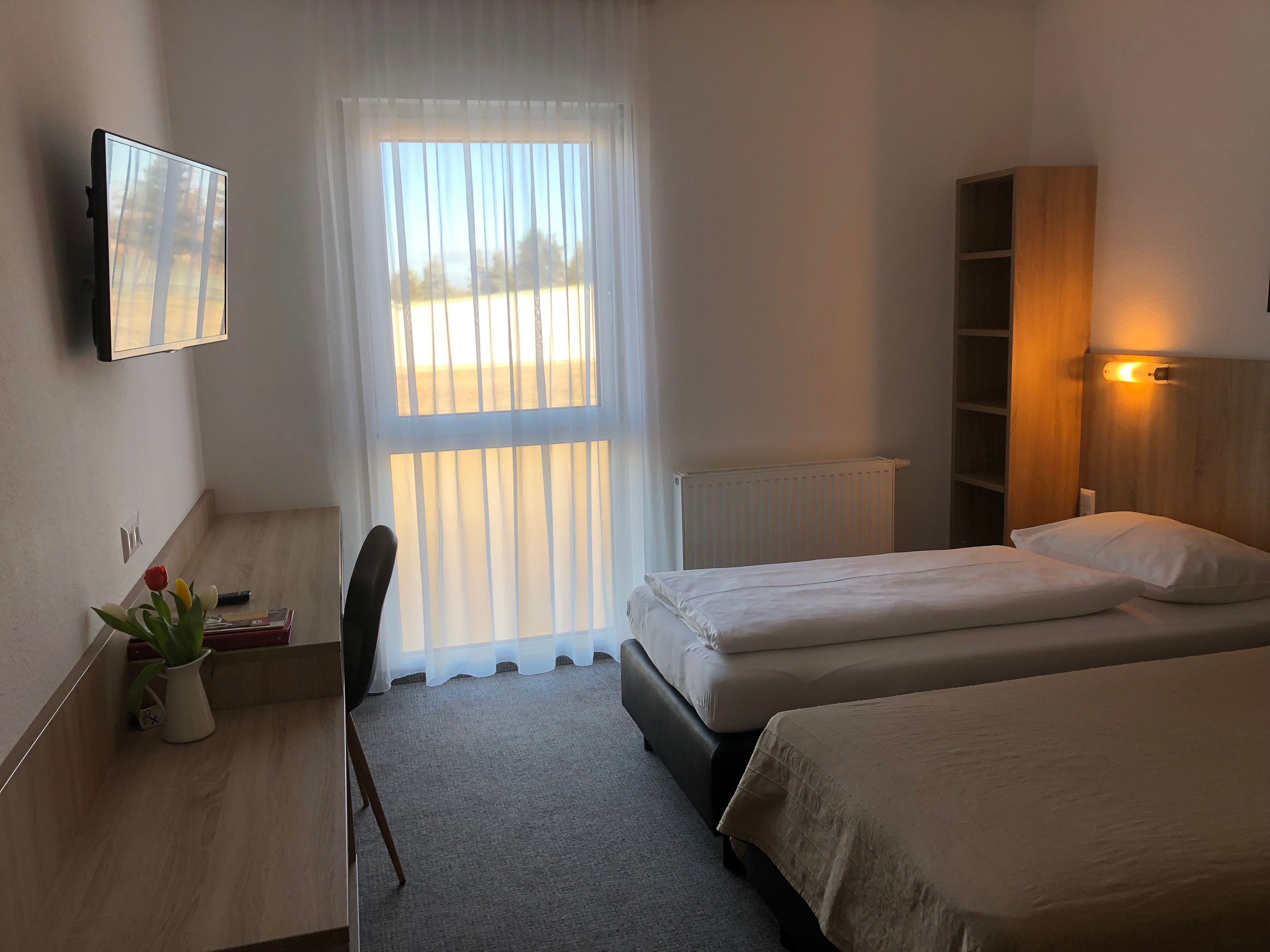 A simply furnished motel room with two single beds, a desk, a TV and a window with curtains.