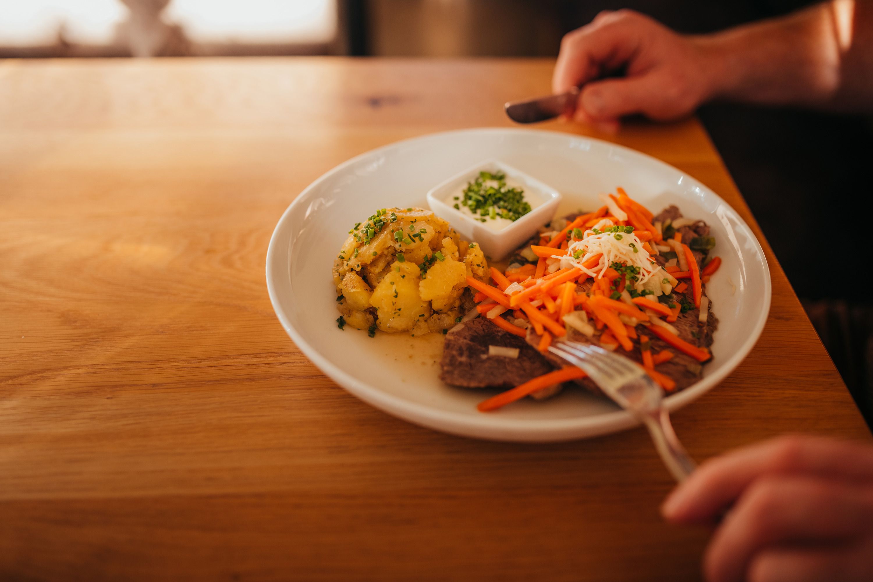 Plate with meat, carrots, potatoes and dip on wooden table.