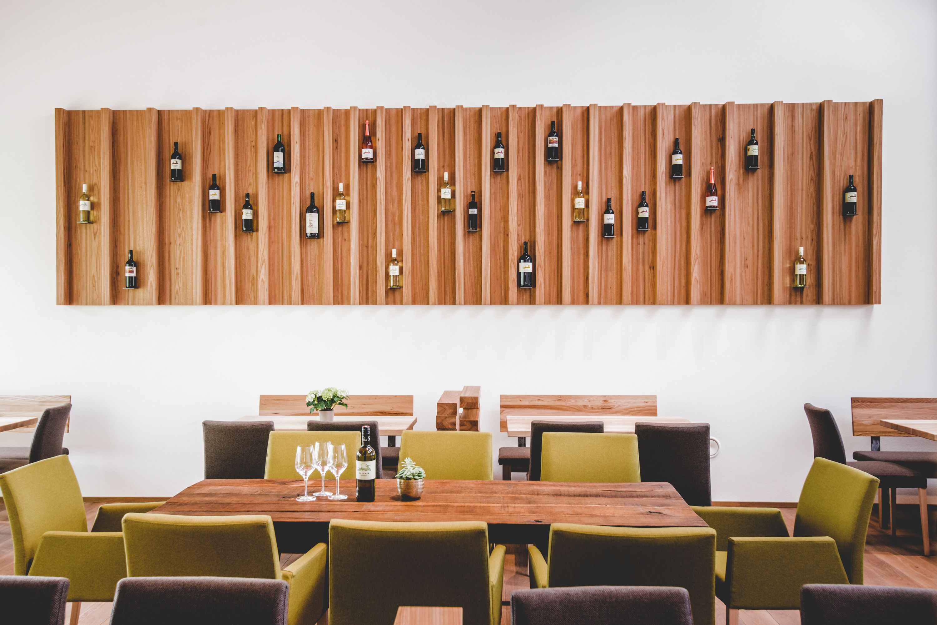 Interior view of a modern wine tavern with wooden tables and wine bottles on the wall.