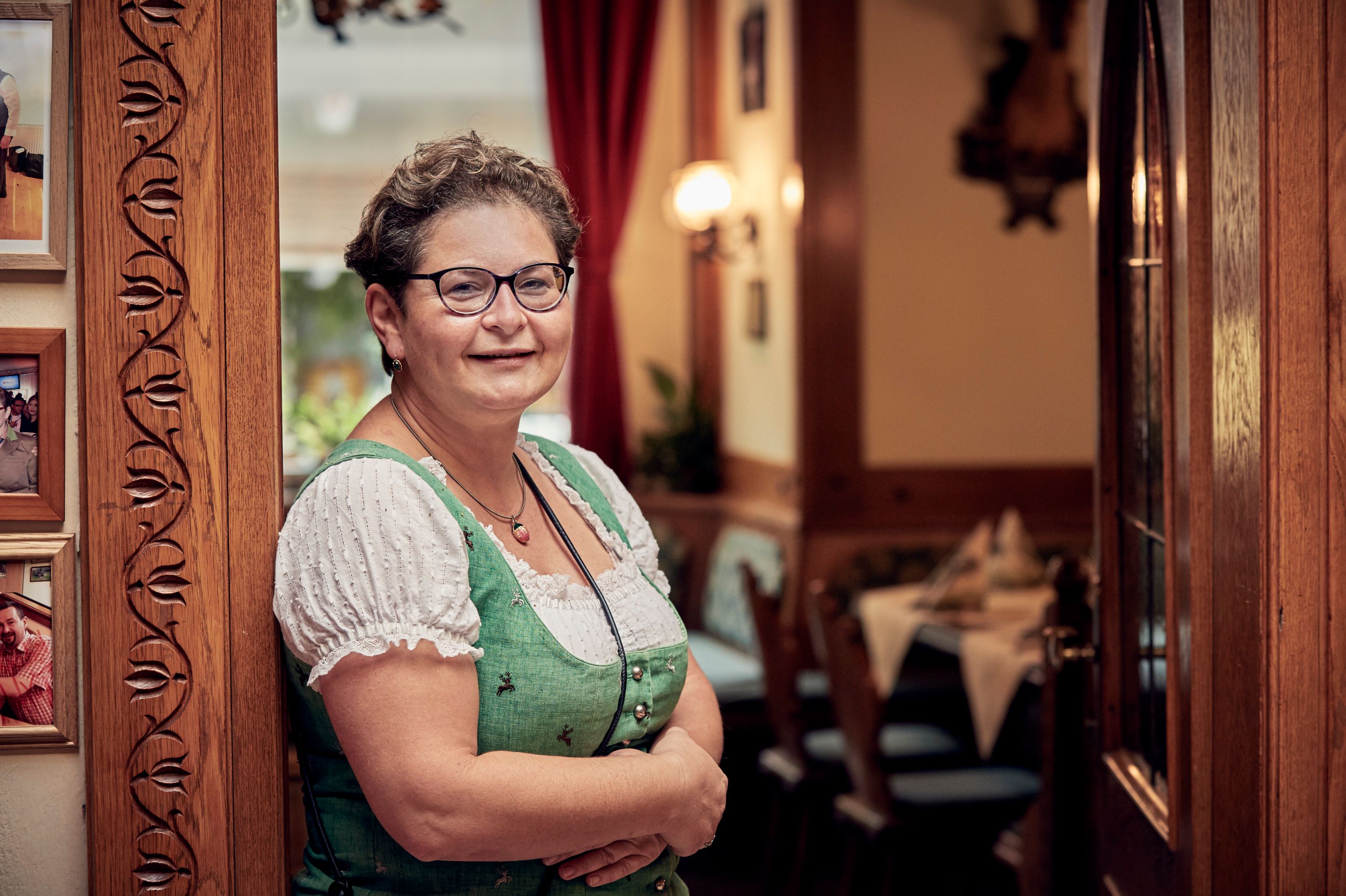 A woman in traditional dress stands smiling in a cozy dining room.