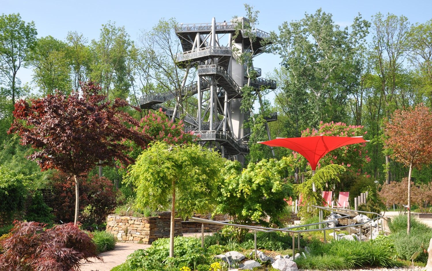 A treetop walk with a high, modern metal tower in a green wooded area.