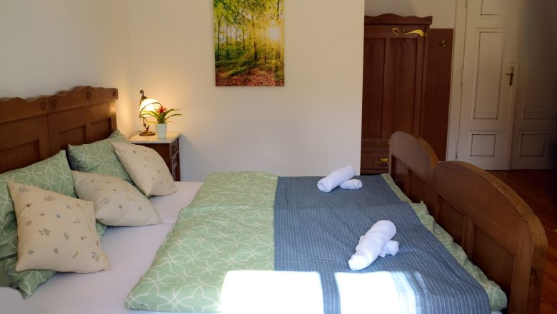 Cozy double room with wooden furniture, green bedding and a picture on the wall.