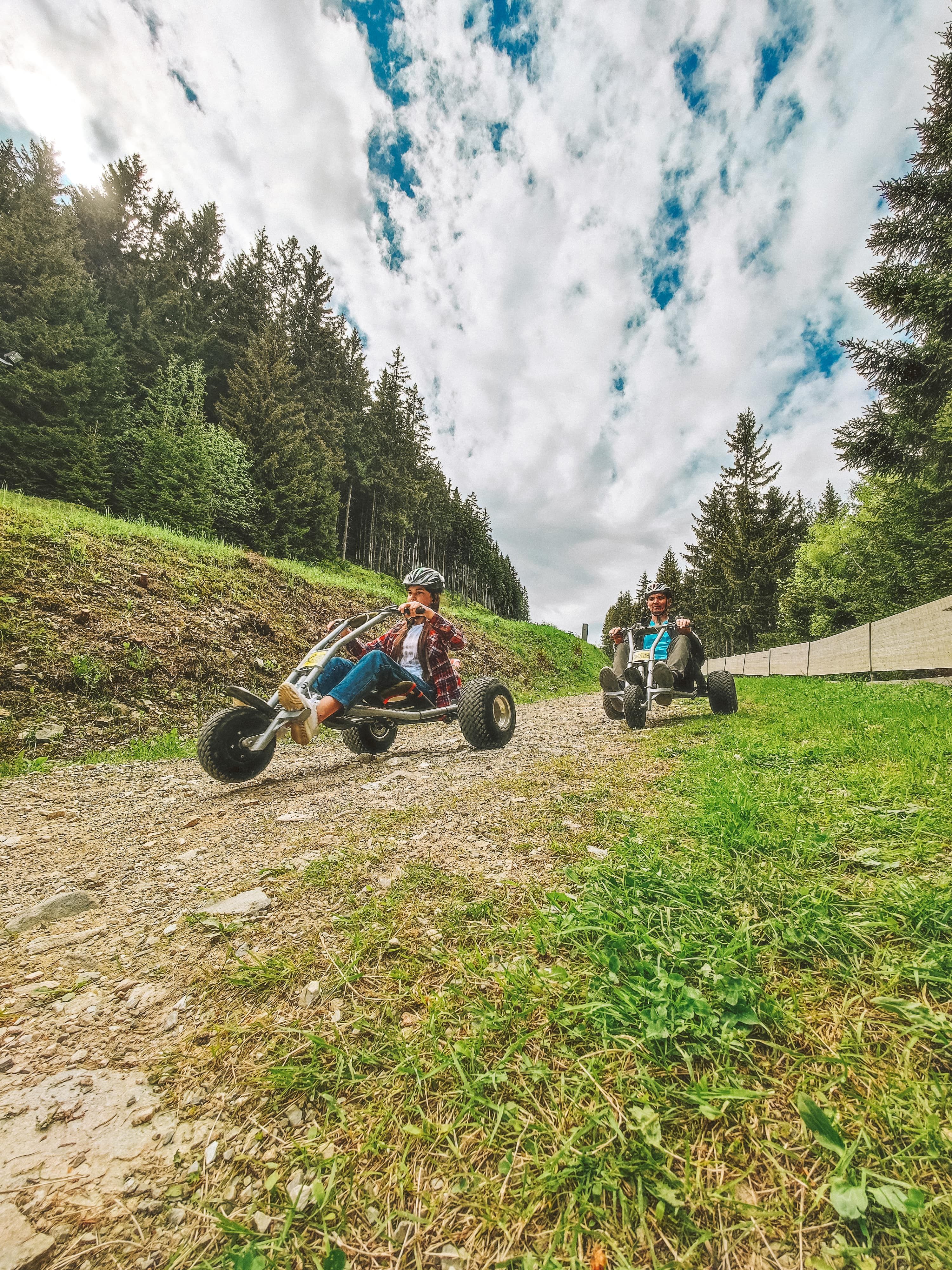 Two people are riding mountain carts on a gravel path in the forest.