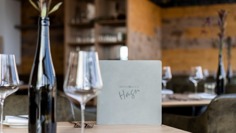 A set table in a restaurant with wine glasses, a bottle of wine and a menu.