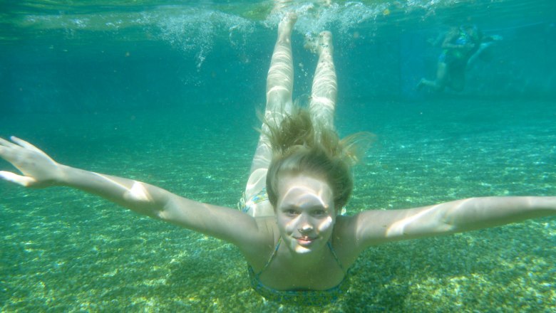 Underwater shot of a girl swimming in a clear natural pool.