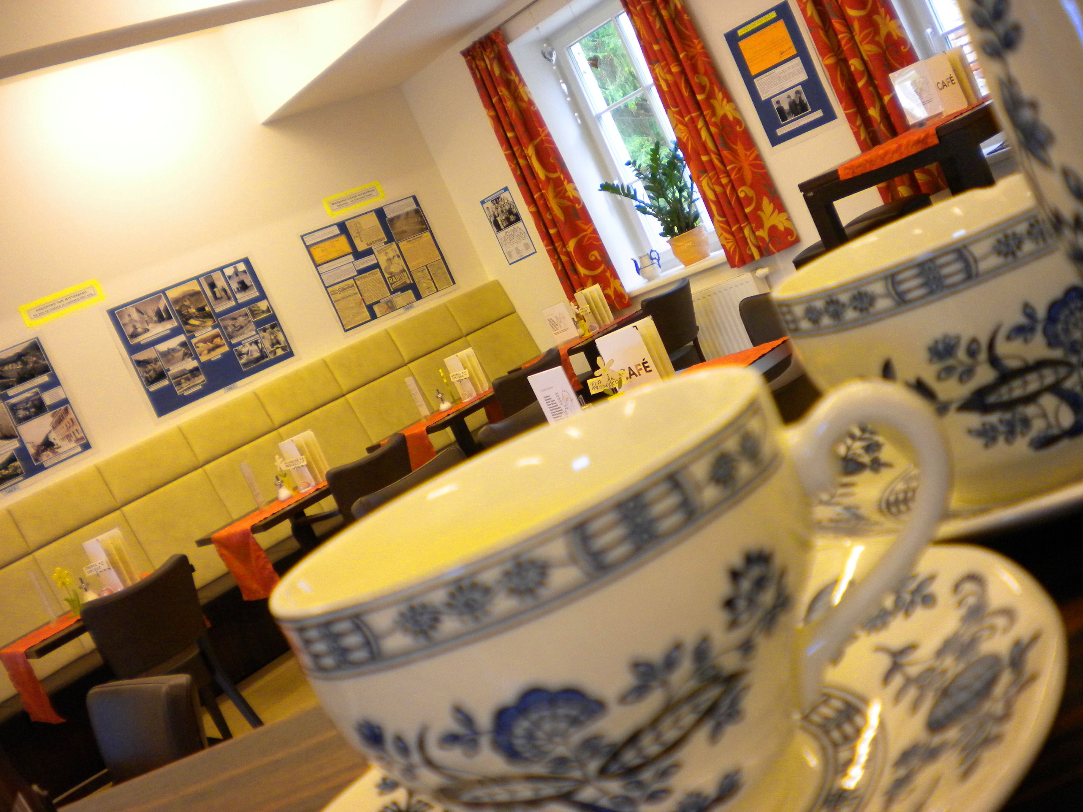 Interior view of a café with teacups in the foreground and decorated walls in the background.